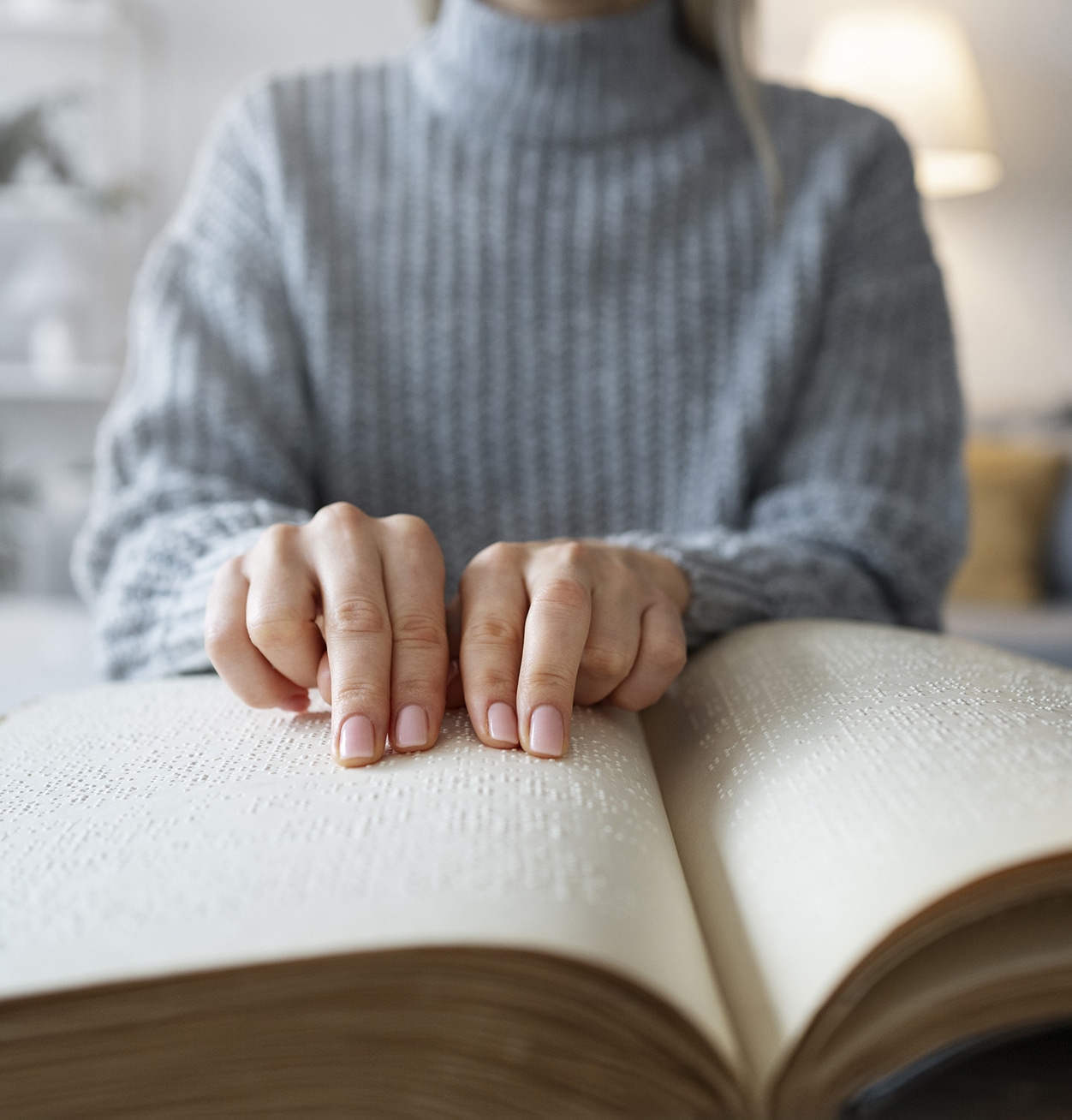 Frauenhände ertasten die Seiten eines dicken Buches, dessen Inhalt in Brailleschrift gedruckt ist.