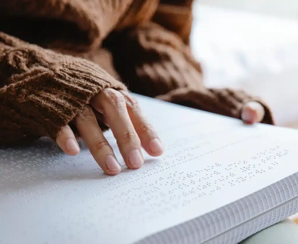 Detailaufnahme von Händen, die die Seiten eines Hardcover Buches ertasten, dessen Inhalt in Brailleschrift gedruckt ist.