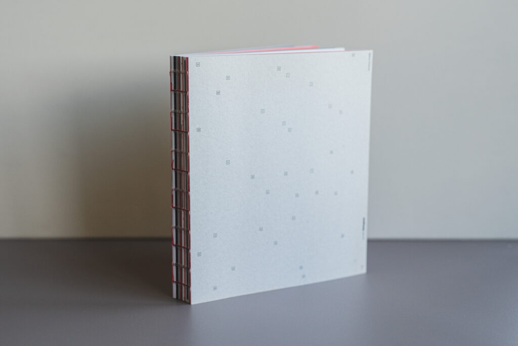 Softcover-Buch mit offener roter Fadenbindung, grauem Kartonumschlag und gedrucktem Innenteil auf Naturpapier