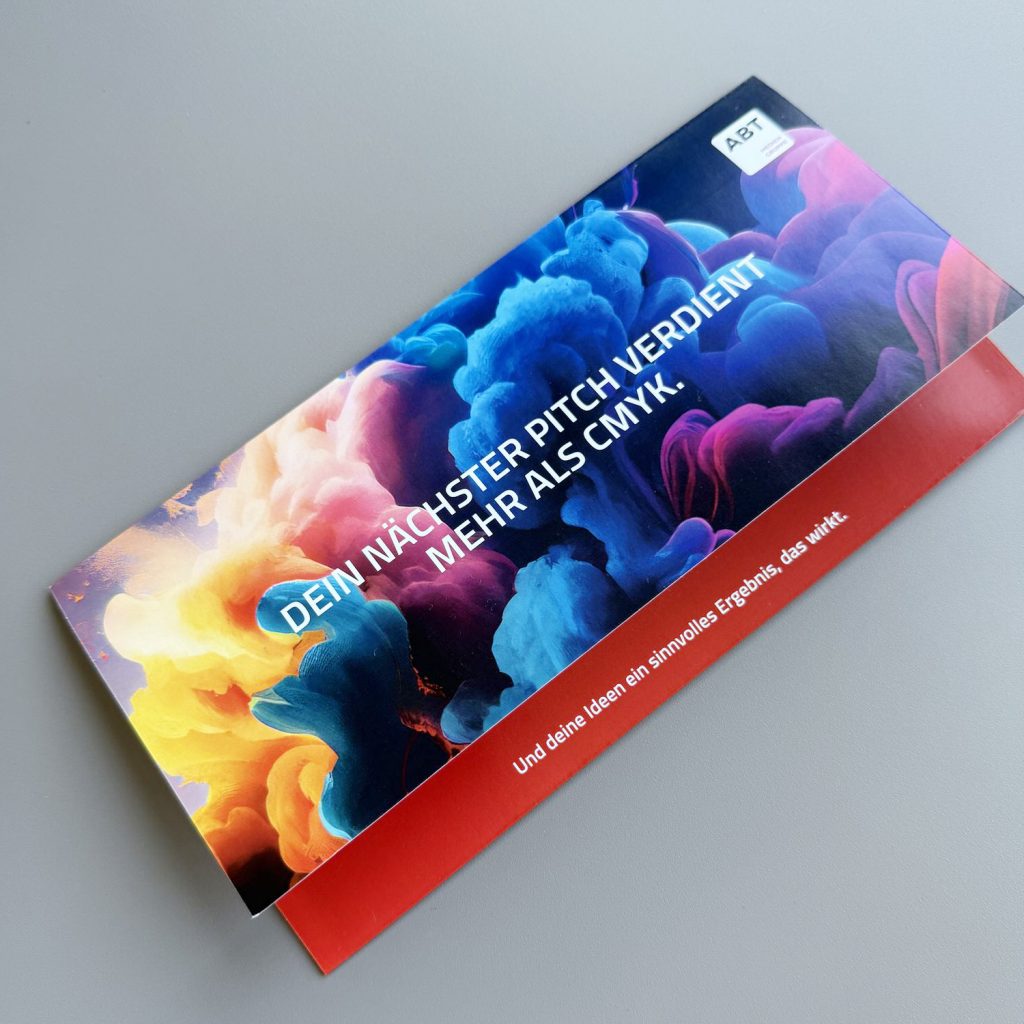 Schräg liegender Selfmailer mit farbigem Wolkenmotiv und Werbebotschaft auf grauem Hintergrund