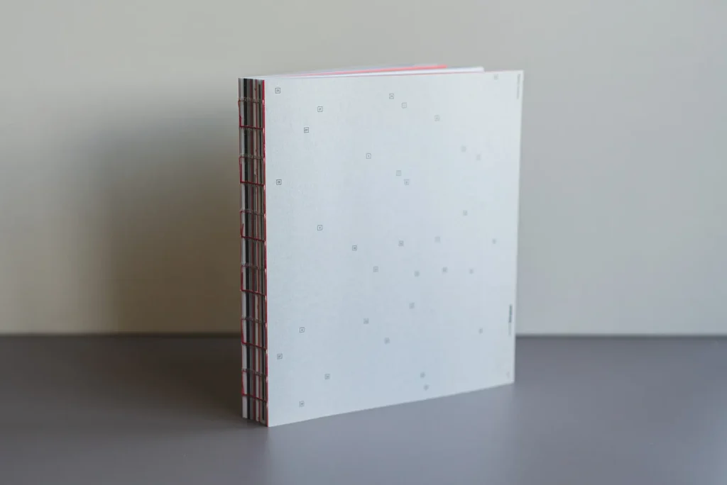Softcover-Buch mit offener roter Fadenbindung, grauem Kartonumschlag und gedrucktem Innenteil auf Naturpapier